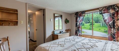 A bedroom with a large bed, a wooden chair, a desk, and a window with curtains.