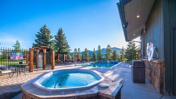 Un bain à remous et deux piscines agrémentées d’une pergola en bois, ainsi qu’un panneau indiquant qu’il n’y a pas de sauveteur en service.