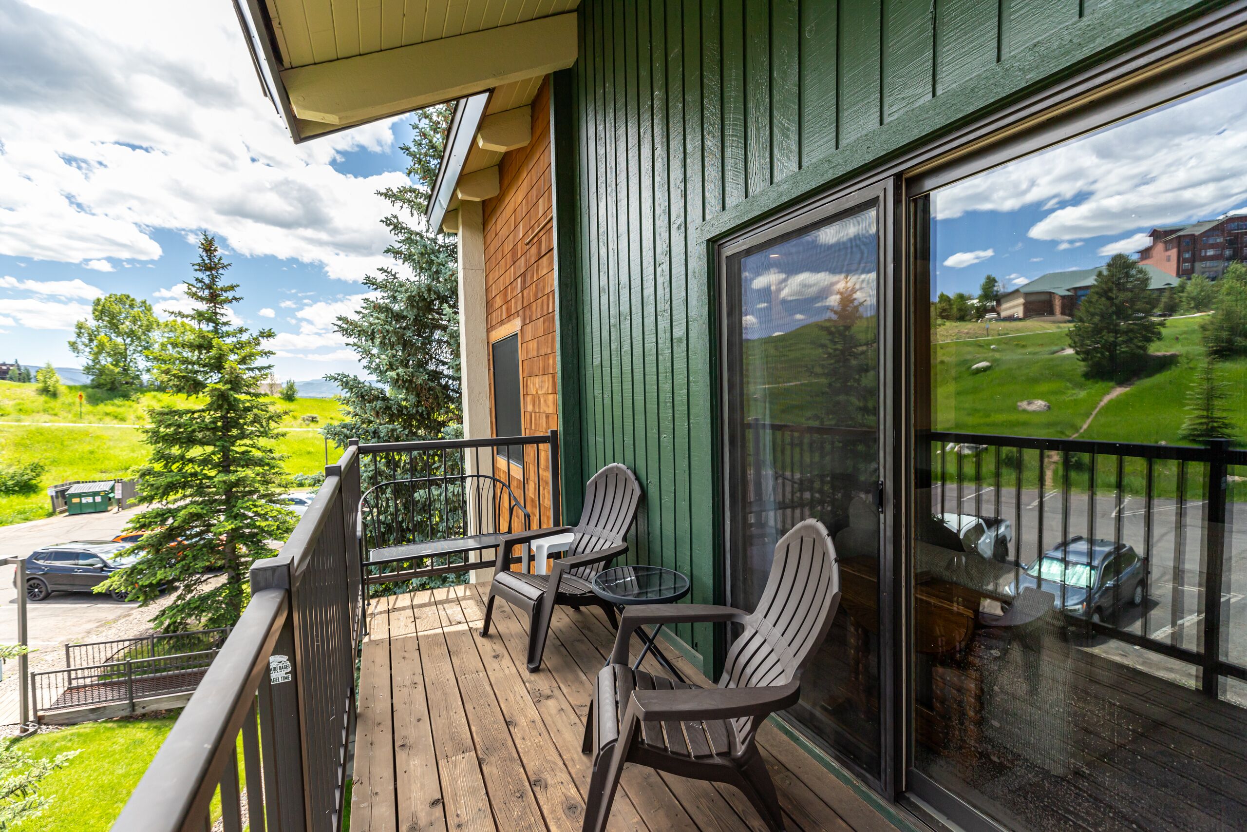 A balcony with wooden flooring, two Adirondack chairs, and a small round table.