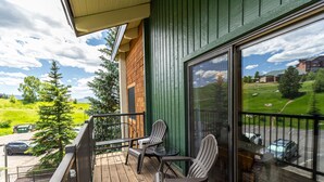 Un balcon doté d’un plancher en bois, de deux fauteuils Adirondack et d’une petite table ronde.