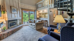 Un salon chaleureux avec une cheminée, des sièges confortables, un escalier et une vue sur l’extérieur.