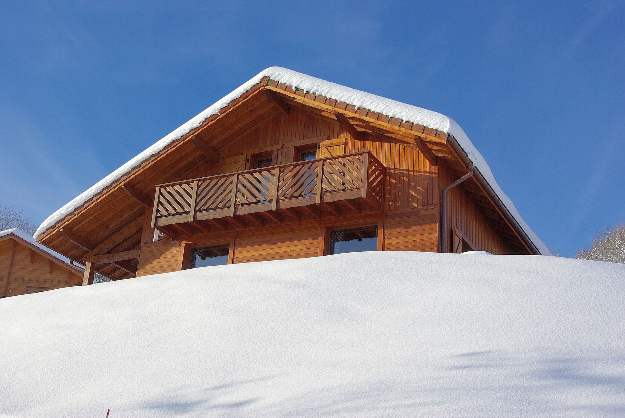 Una cabaña de madera con techo nevado y un balcón.