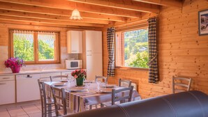 Ein gemütliches Holzhaus mit Essbereich, Küche und einem großen Fenster mit Vorhängen.