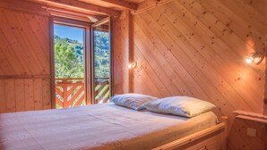 Ein Schlafzimmer einer Holzhütte mit einem Bett, einem Nachttisch und einem Fenster mit Blick auf einen bewaldeten Hügel.