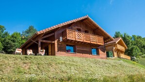 Eine Holzhütte mit einem Balkon, auf einem grasbewachsen Hügel gelegen.