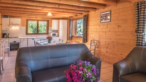 Ein gemütliches Blockhaus-Interieur mit Essbereich, Küche und einer schwarzen Ledersofa mit Blumenarrangement.