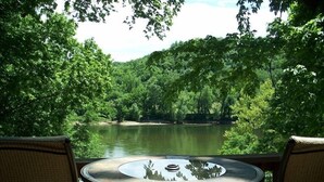 Een ronde tafel met stoelen gericht op een rivier, omgeven door weelderige begroeiing.