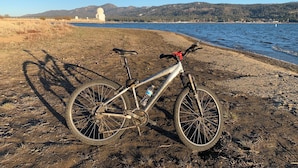 Una bicicleta estacionada en un sendero de tierra junto a un lago, con montañas al fondo.