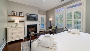 A bedroom with a bed, a dresser, a television, a fireplace, and large windows. - 3 BR/2.5 BA Family Friendly Villa! Golf Views! Amenities included! (Seabrook Island)