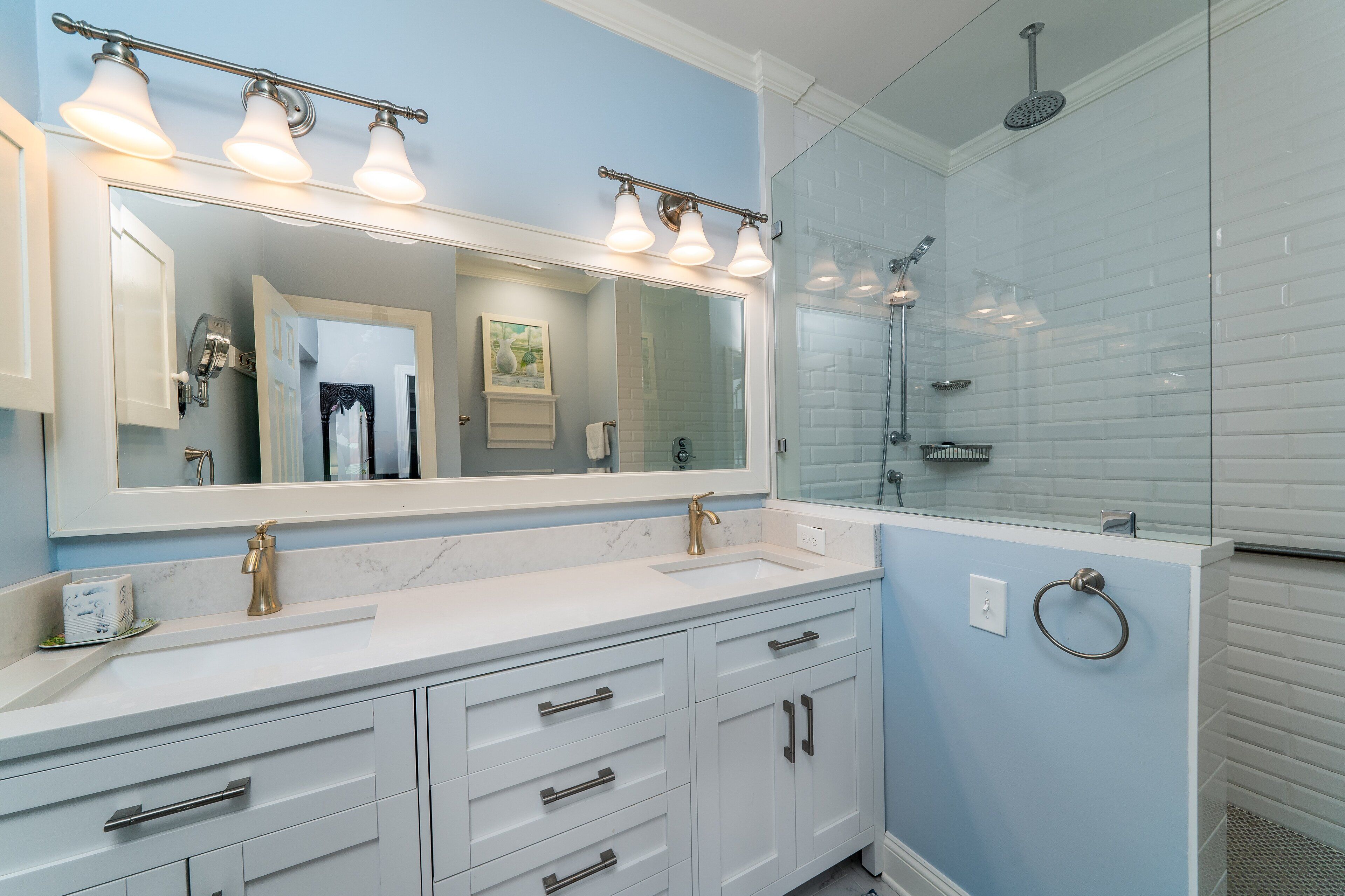 Une salle de bain dotée d’un grand miroir, d’un meuble-lavabo blanc et d’une cabine de douche en verre.