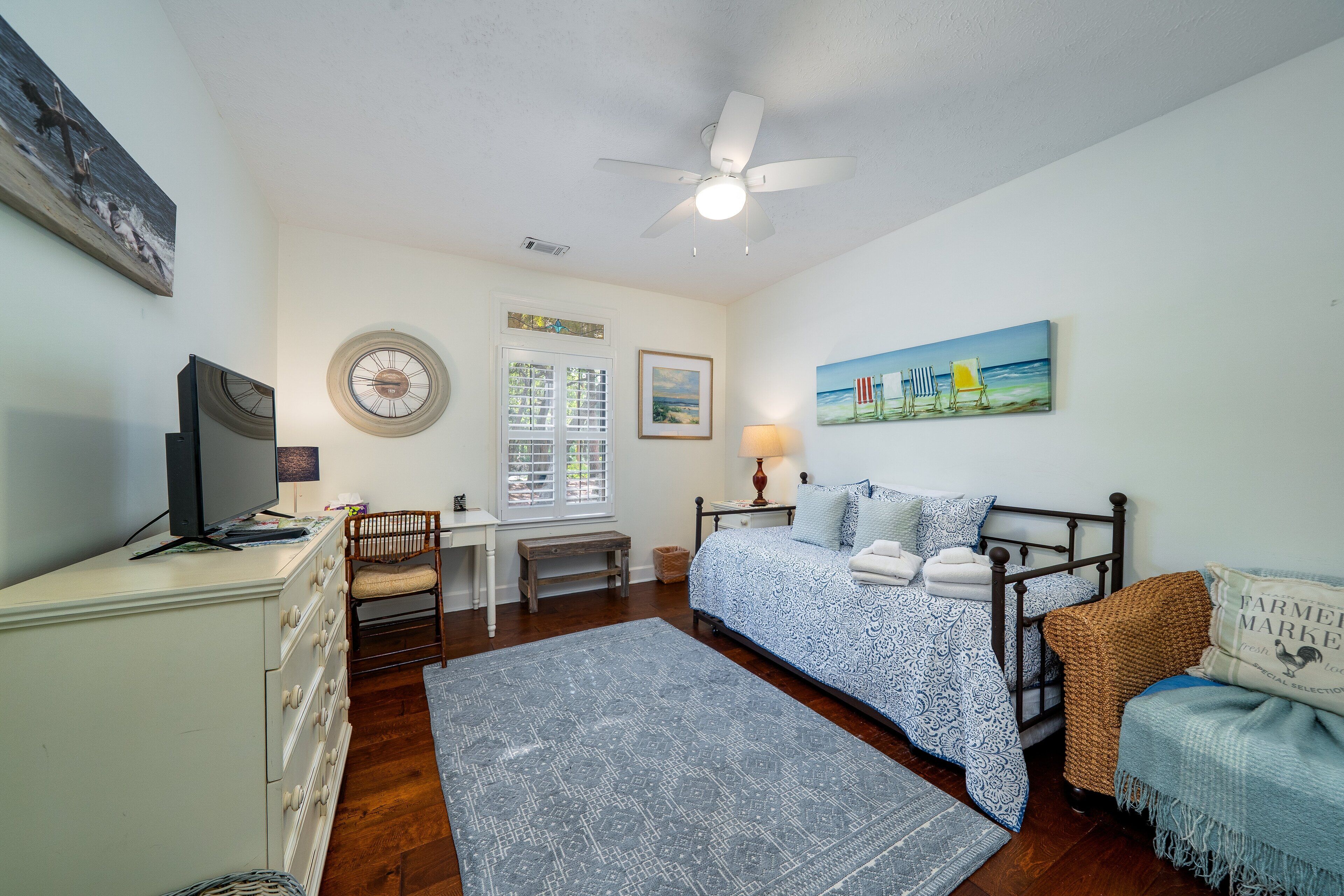 A bedroom with a bed, a desk, a chair, a window, and a ceiling fan.