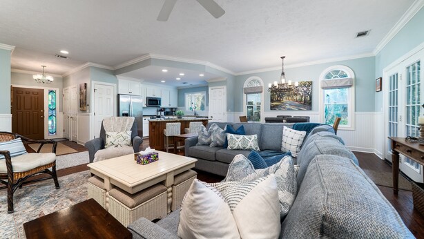 A spacious living room with a gray sectional sofa, a wooden coffee table, and a dining area with a chandelier. - 3 BR/2.5 BA Family Friendly Villa! Golf Views! Amenities included! (Seabrook Island)