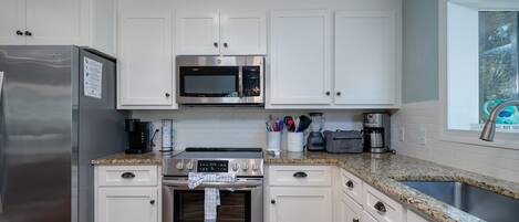 Una cocina moderna con armarios blancos, electrodomésticos de acero inoxidable y encimera de granito.