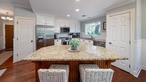 A modern kitchen with white cabinets, stainless steel appliances, and a granite island with wicker chairs. - 3 BR/2.5 BA Family Friendly Villa! Golf Views! Amenities included! (Seabrook Island)