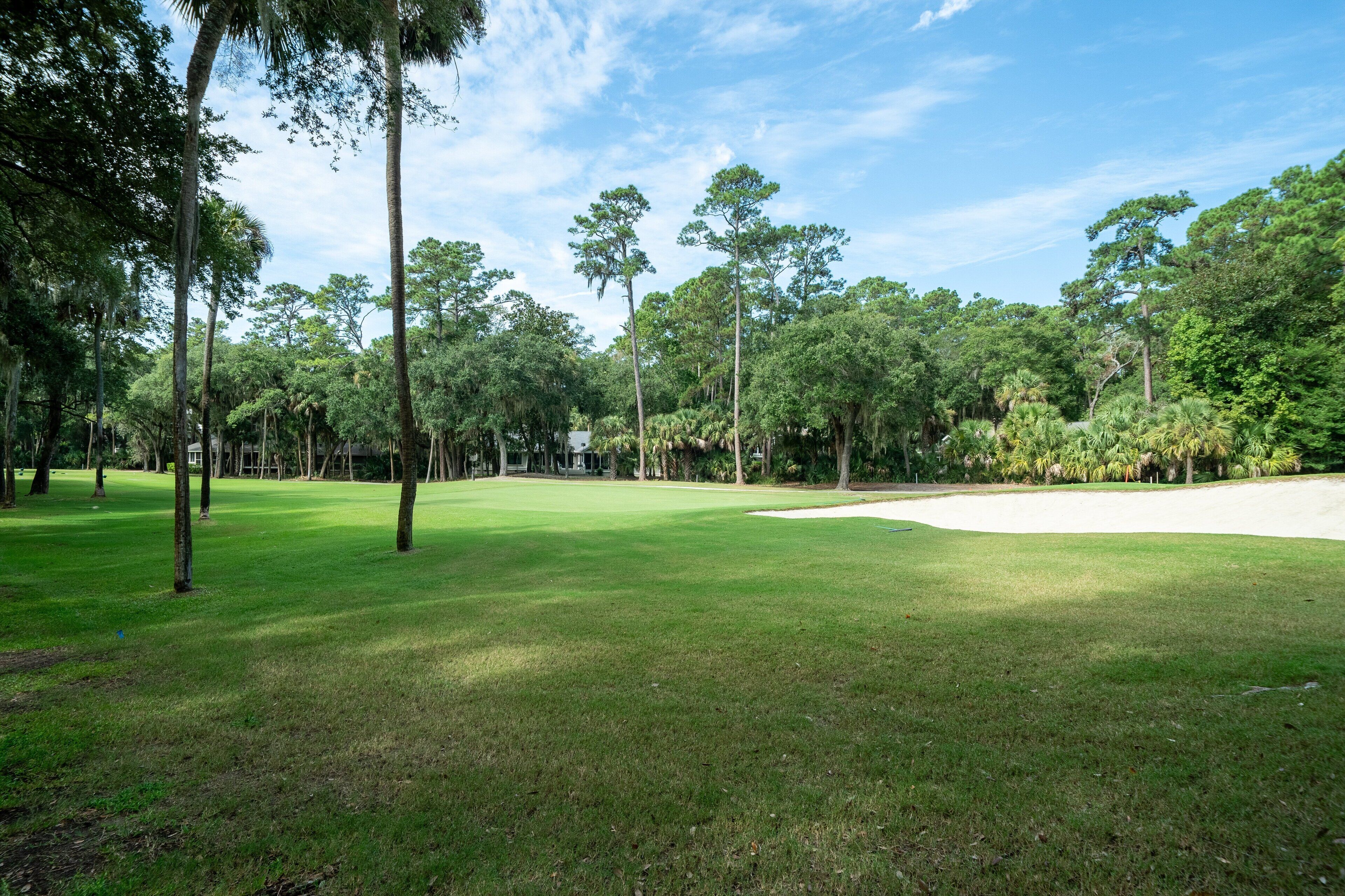 Ein Golfplatz mit gepflegtem Grün, Sandbunkern und hohen Bäumen.