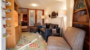 Een knusse woonkamer met een bank, fauteuils, een houten boekenkast en een kamerbreed tapijt.