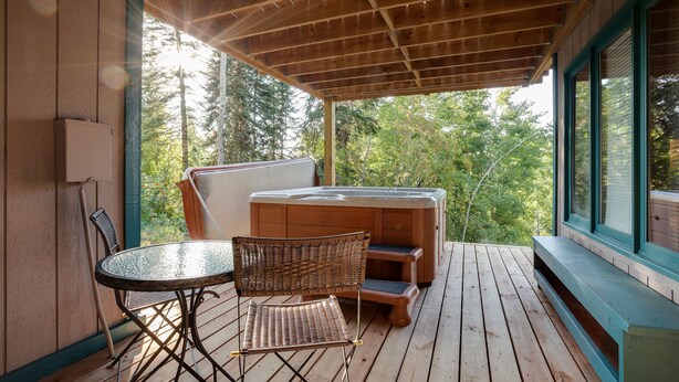 Een houten terras met een jacuzzi, een tafel en stoelen.