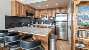 A modern kitchen with wooden cabinets, stainless steel appliances, a marble island, and bar stools.