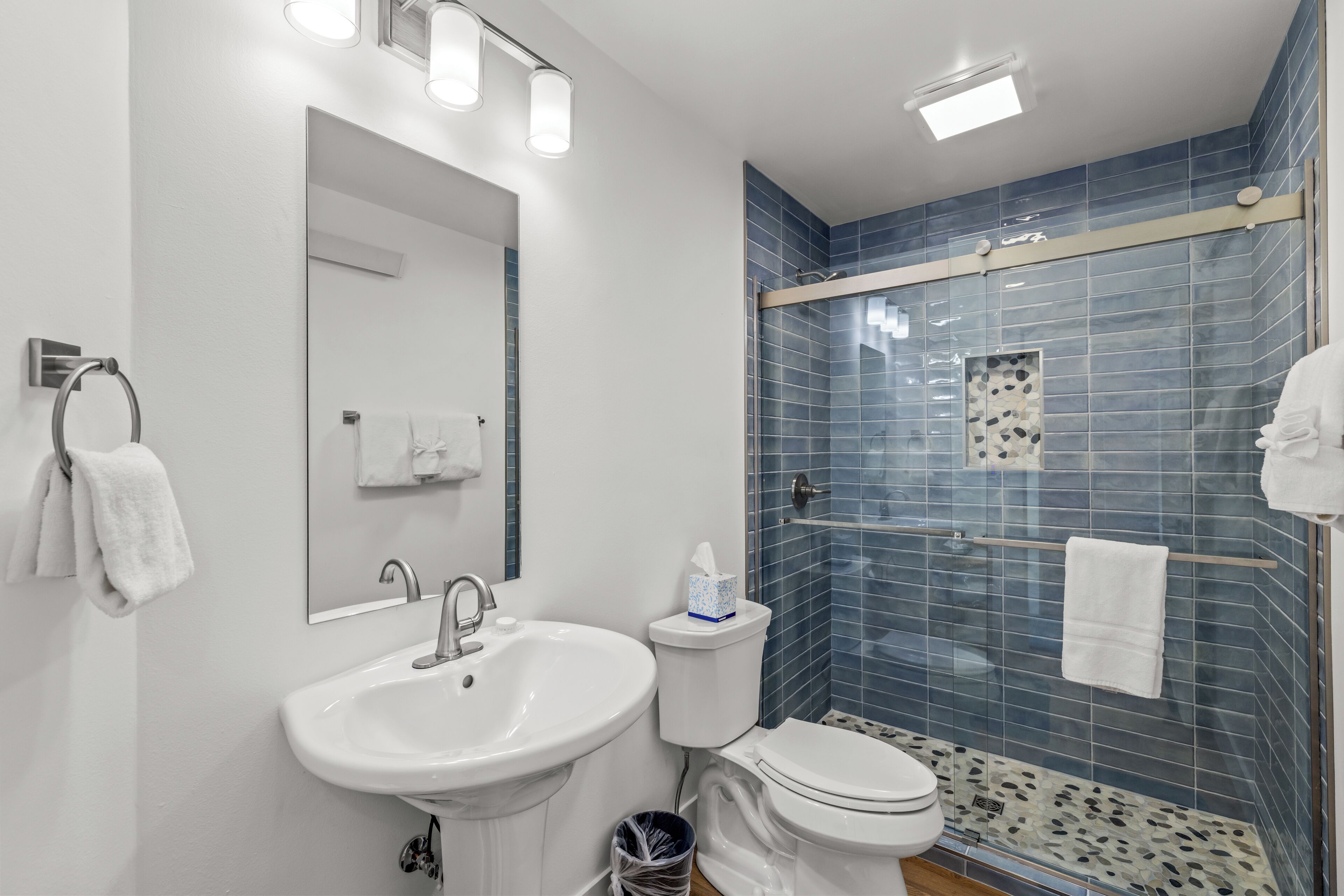 A modern bathroom with a white sink, toilet, and glass-enclosed shower.