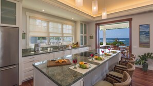A modern kitchen with a large island, white cabinetry, and a view of the ocean. - Designer Two Bedroom | Directly Beachfront | AC | Gourmet Kitchen | Private (Waialua)