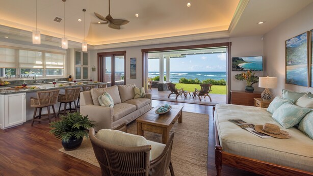 A spacious living area with a large window, a sofa, a coffee table, and a dining area with chairs. - Designer Two Bedroom | Directly Beachfront | AC | Gourmet Kitchen | Private (Waialua)