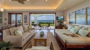 A spacious living room with a large window, a ceiling fan, and a view of the ocean. - Designer Two Bedroom | Directly Beachfront | AC | Gourmet Kitchen | Private (Waialua)