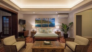 A bedroom with a large bed, two bedside tables, a TV, and a painting on the wall. - Designer Two Bedroom | Directly Beachfront | AC | Gourmet Kitchen | Private (Waialua)