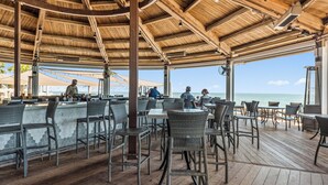 A covered outdoor seating area with wicker chairs and tables, overlooking the beach.