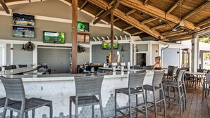 A covered outdoor bar area with a hexagonal tile backsplash, wicker bar stools, and a counter with a cash register.