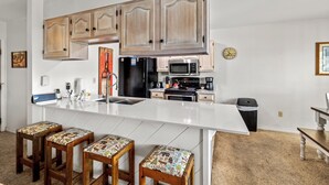 A kitchen with wooden cabinets, a white countertop, and three stools with patterned cushions. - Cozy 2-Bedroom Ground-Floor Condo at The Phoenix – Steps from the Slopes! (Steamboat Springs)