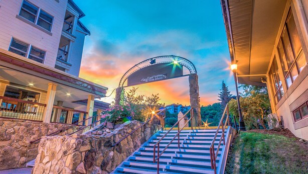 Entrada de hotel com escadaria de pedra, corrimão de metal e placa sobre a entrada.