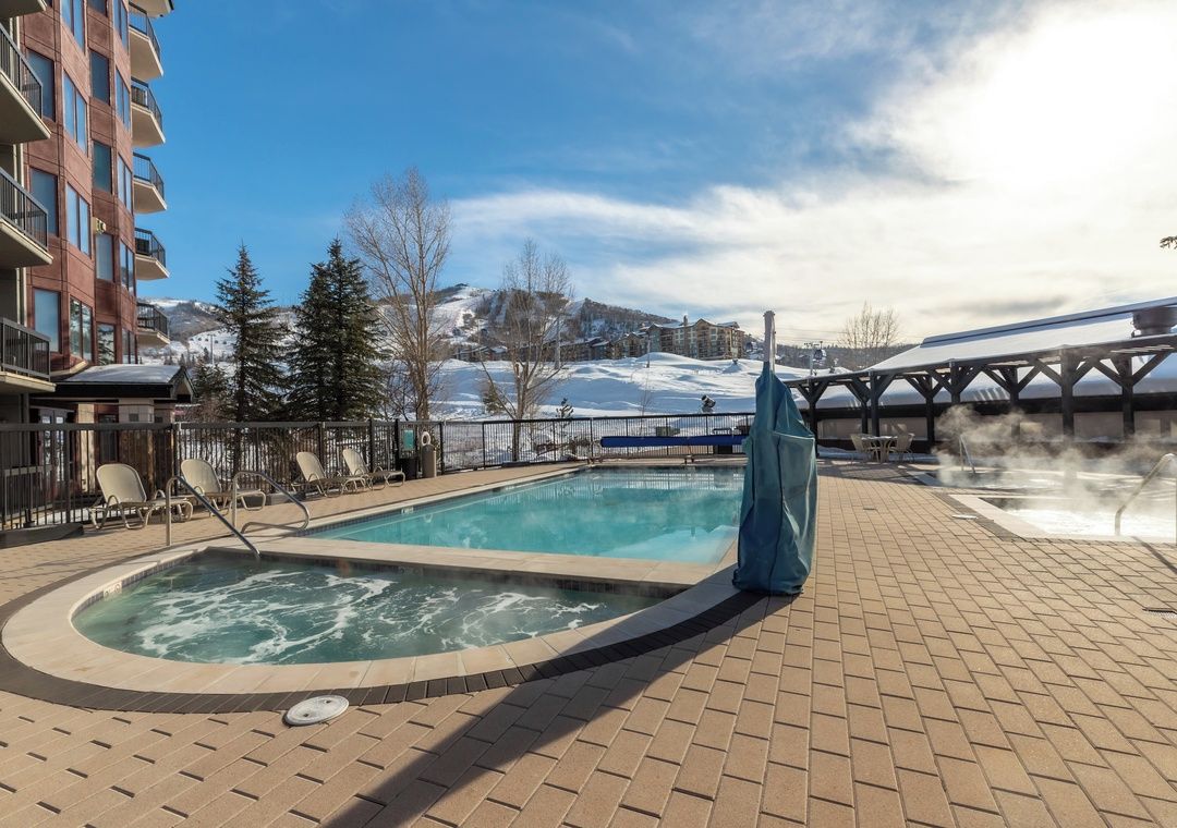 A pool area with a hot tub, lounge chairs, and a view of a snowy mountain.