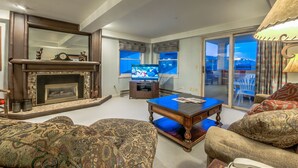 Uma sala de estar com lareira, televisão e vista através de uma porta de vidro.