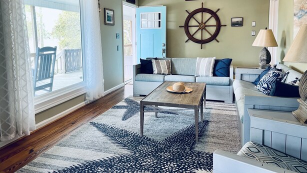 Uma sala de estar com sofá, mesa de centro e um leme fixado na parede.