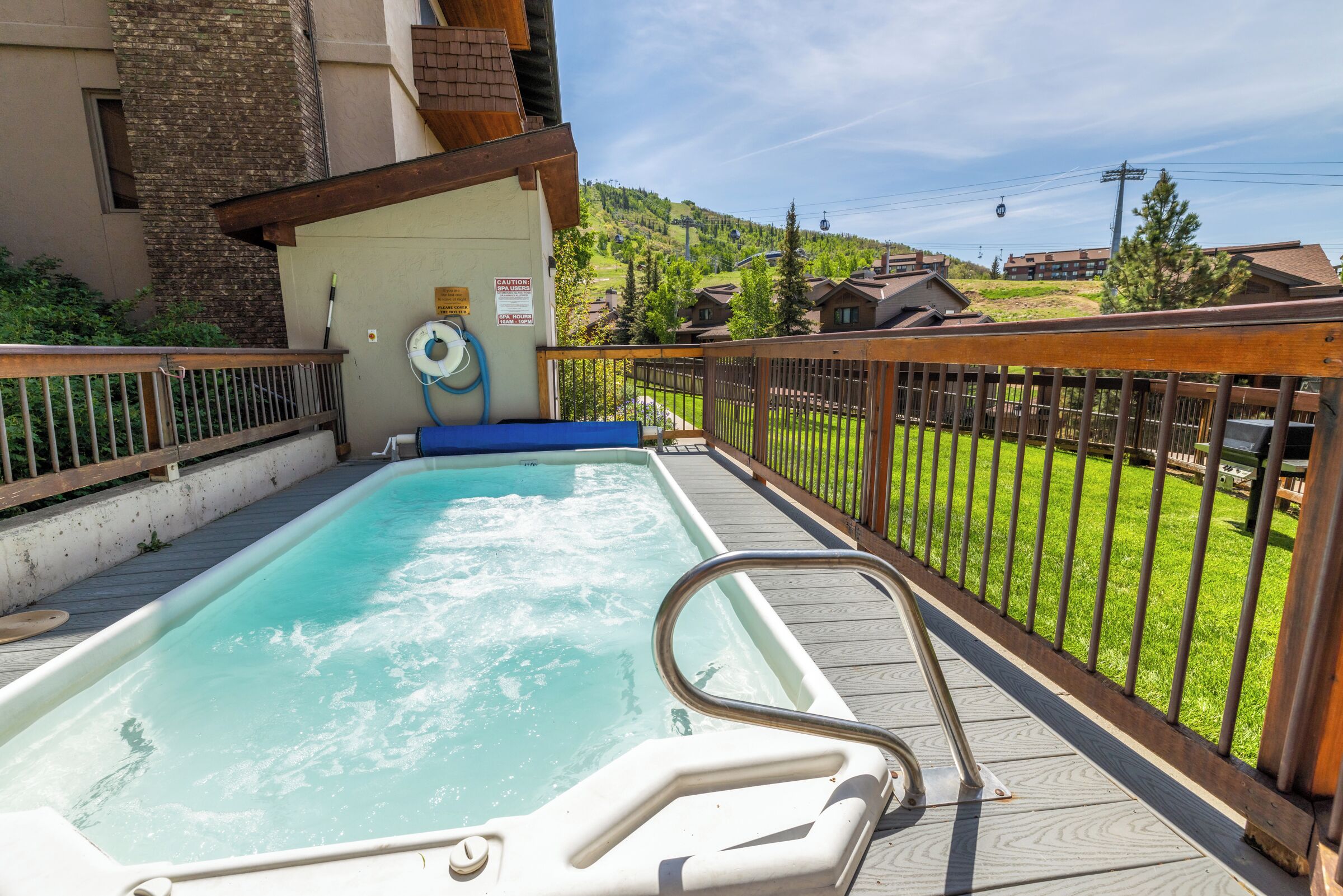 A hot tub on a wooden deck with a view of a hillside and buildings in the background.