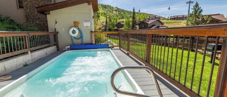 A hot tub on a wooden deck with a view of a hillside and buildings in the background.