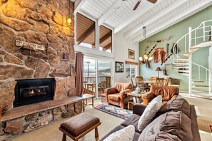 A cozy living room with a stone fireplace, leather furniture, and a spiral staircase. - Slopeside Ski Getaway | Fireside + Hot Tub (Steamboat Springs)