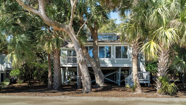 Ein strandnahes Anwesen mit einem zweigeschossigen Haus, einer überdachten Terrasse und einer Treppe, die zum oberen Stockwerk führt.