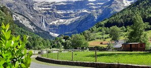 A rural landscape with a mountain backdrop, a small wooden cabin, and a fenced area with greenery. - Hôtel Vignemale (Gavarnie-Gedre)
