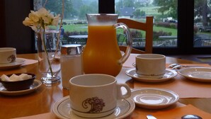 A breakfast setup with a pitcher of orange juice, a vase with a white flower, and a scenic mountain view through a window. - Hôtel Vignemale (Gavarnie-Gedre)