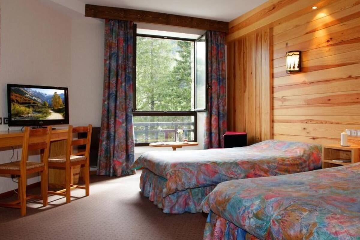 A room with two beds, a desk with a chair, a television, and a window with curtains.