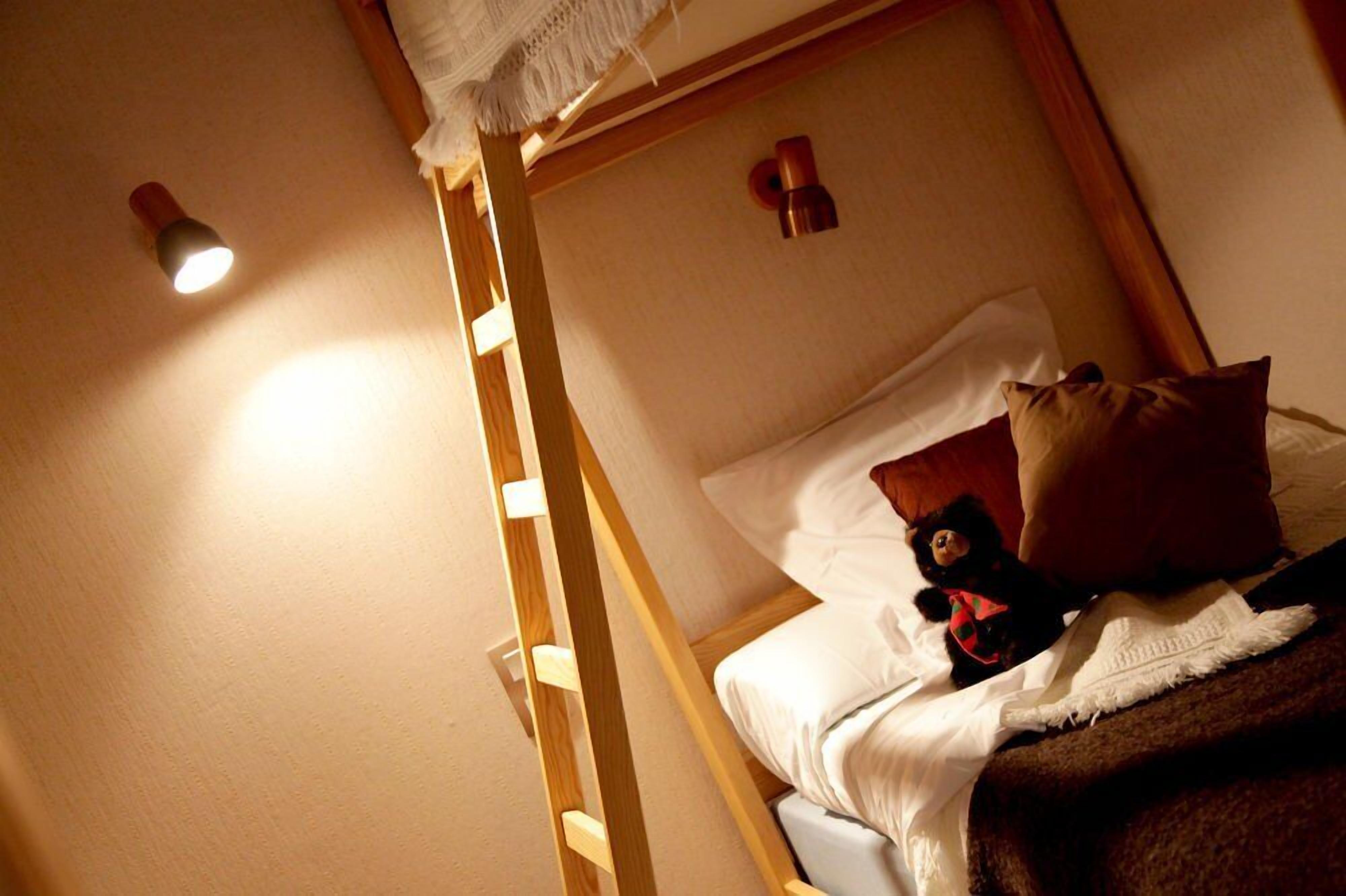 Una cama litera con escalera, un oso de peluche y una almohada blanca.