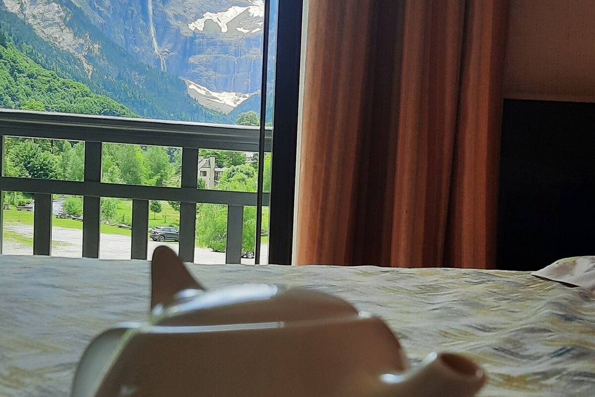 A teapot on a tray on a table with a view of a mountainous landscape through a window.