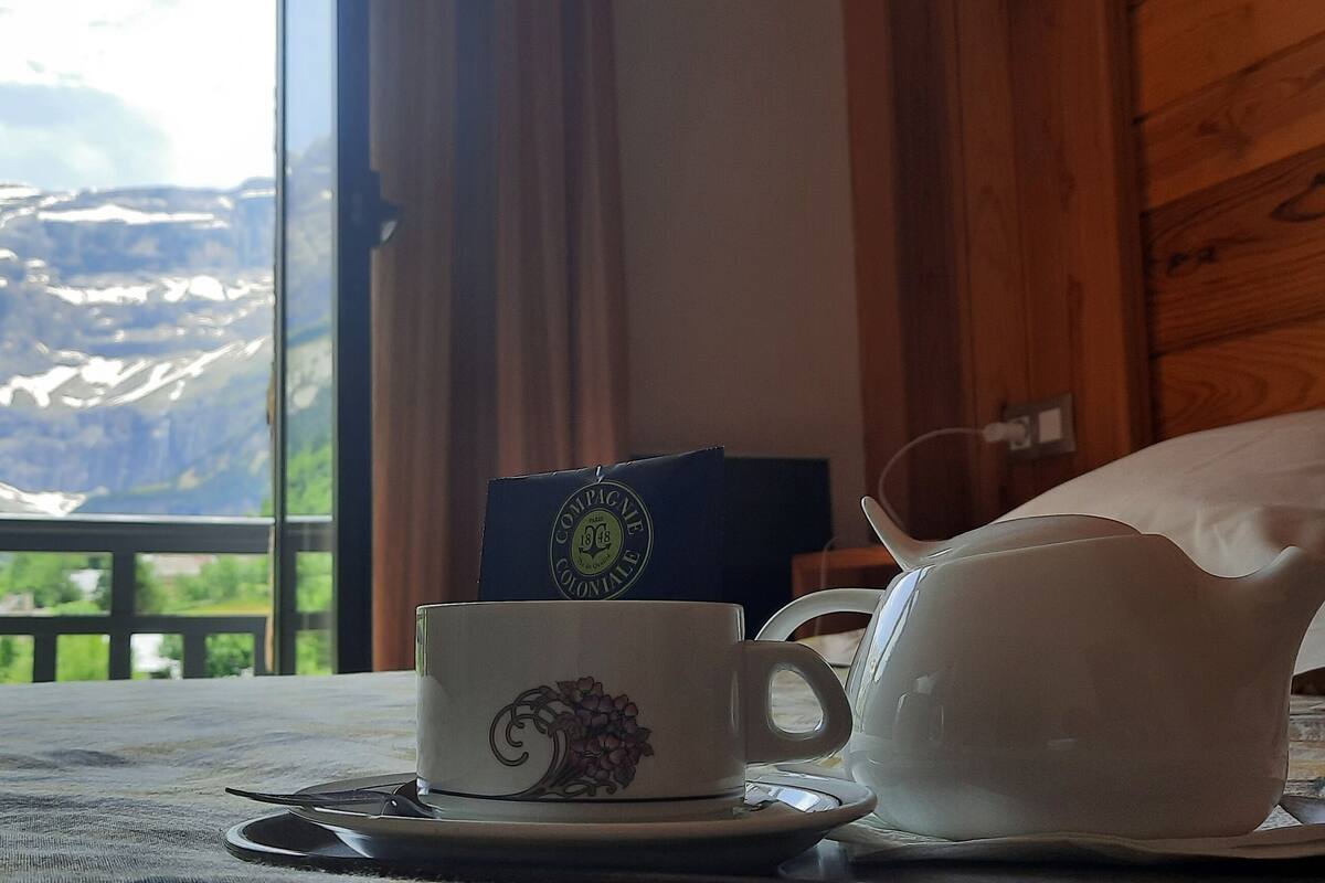 A table with a cup and saucer, a teapot, and a booklet, with a mountainous view through a window.