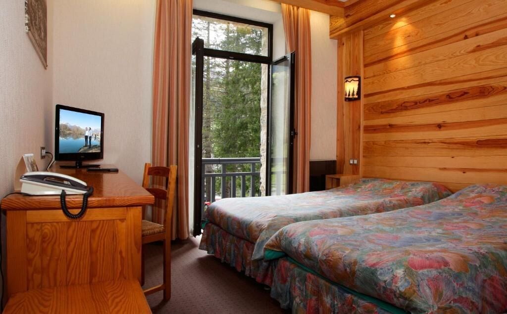 A hotel room with a wooden interior, a desk with a telephone, a television, and two beds with floral bedding.
