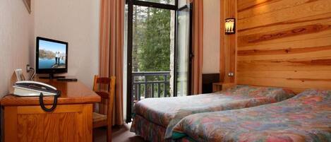 A hotel room with a wooden interior, a desk with a telephone, a television, and two beds with floral bedding.