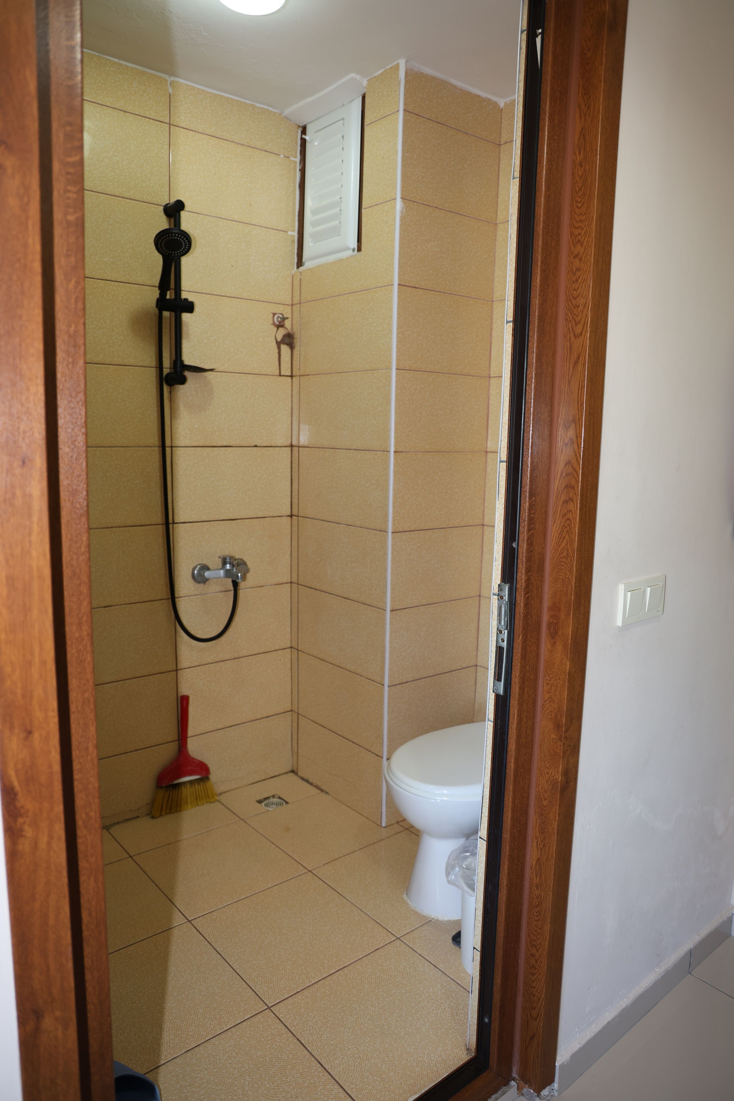 A bathroom with a shower, toilet, and a broom.