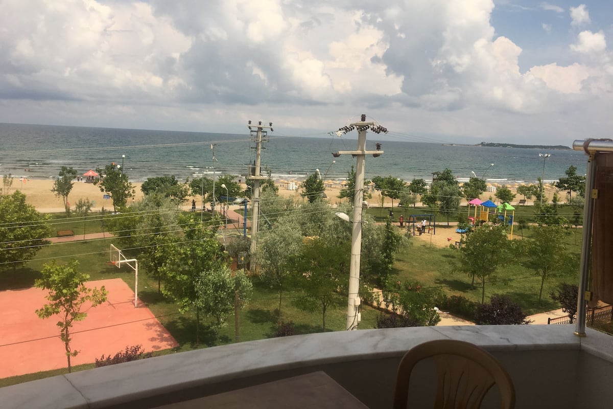 A beach view from a balcony with a clear sky, power lines, and a playground.
