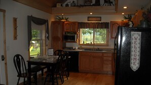 A kitchen with wooden cabinets, a refrigerator with a welcome sign, a dining table with chairs, and a view of the outdoors through the windows.