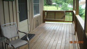 A wooden porch with a bench and a chair, a door with a sign, and a view of a green landscape.